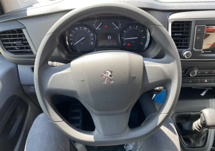 Vue intérieure centrée sur le volant Peugeot gris avec tableau de bord et levier de vitesses manuel visibles.
