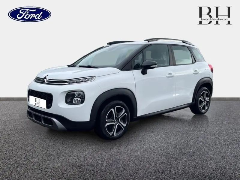 Citroën C3 Aircross blanc Natural White vue 3/4 avant droit avec barres de toit et jantes noires distinctives.