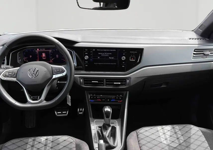 Vue intérieure avant du Volkswagen Taigo blanc 2025, volant multifonction et écran tactile central visible.