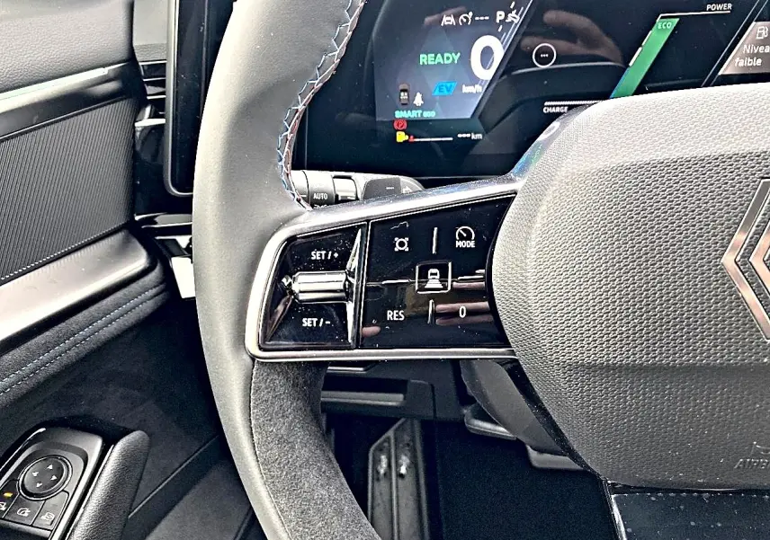 Gros plan sur le volant gris et les commandes multifonctions du Renault Austral 1.2 e-tech hybride, tableau de bord digital en arrière-plan.