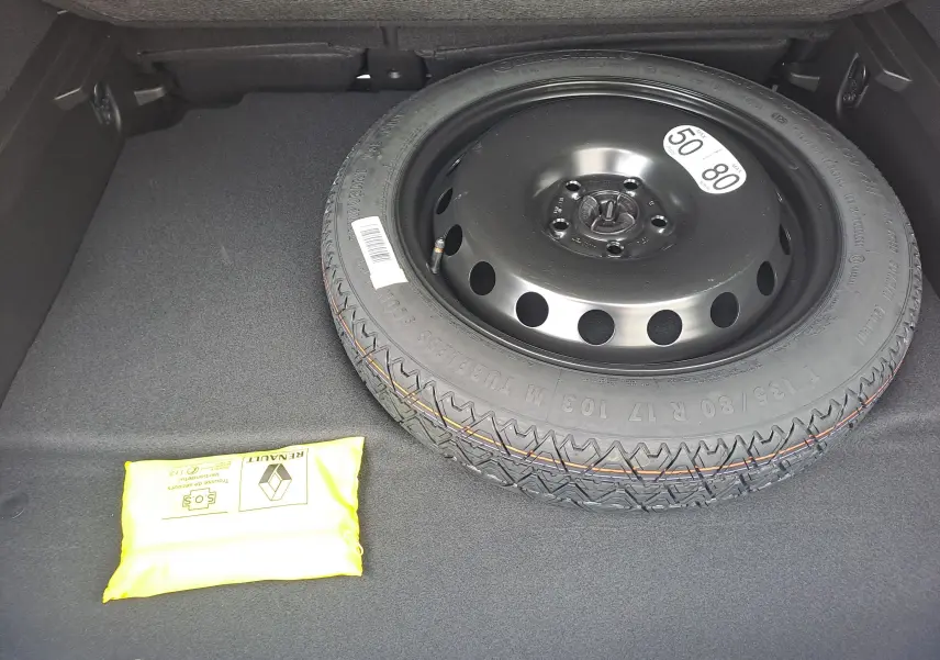 Vue rapprochée du coffre du Renault Symbioz 2025 montrant la roue de secours noire et un kit de sécurité jaune.