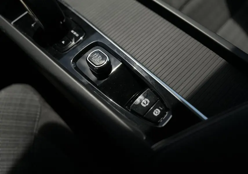 Gros plan sur la console centrale noire de la Volvo S60 rouge Fusion 2024, avec bouton start/stop et frein à main électronique.