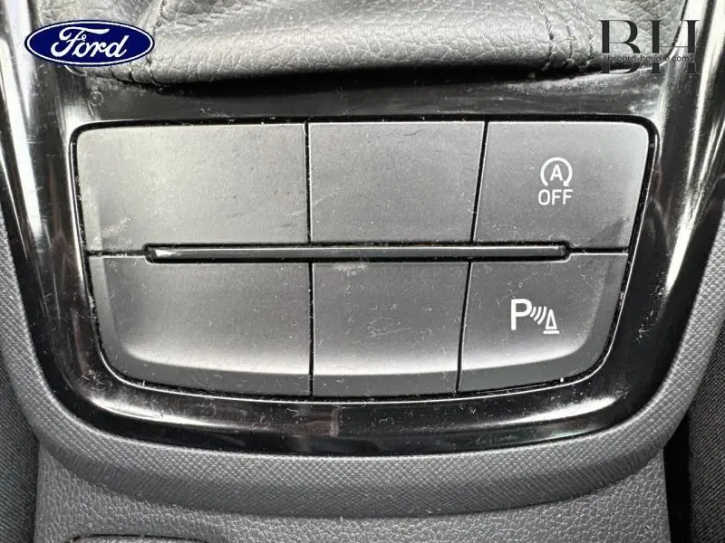 Gros plan sur les boutons de commande noirs du tableau de bord d'un Skoda Kamiq gris graphite 2023, avec fonction arrêt auto et aide au stationnement.