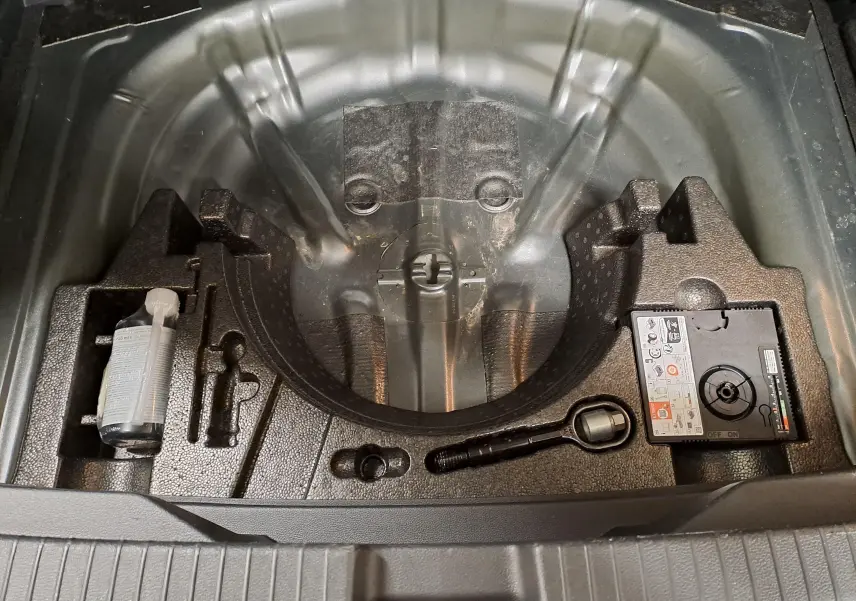 Coffre ouvert du Volkswagen T-Roc 1.5 TSI 2024 montrant le rangement sous plancher avec kit de réparation pneus.