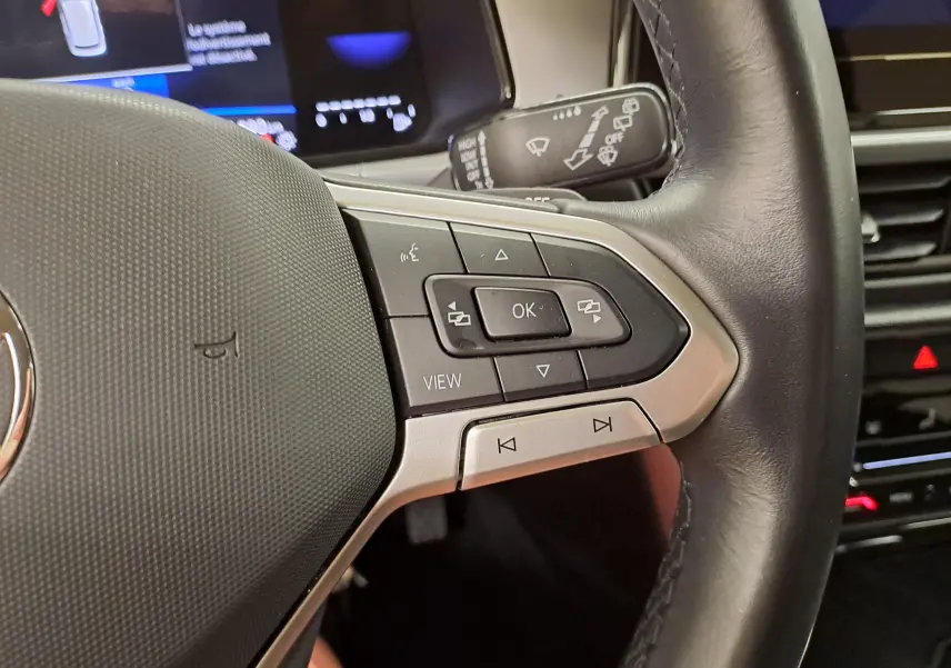 Gros plan sur les commandes à droite du volant en cuir du Volkswagen T-Roc 2024, avec boutons multifonctions et affichage numérique partiel.