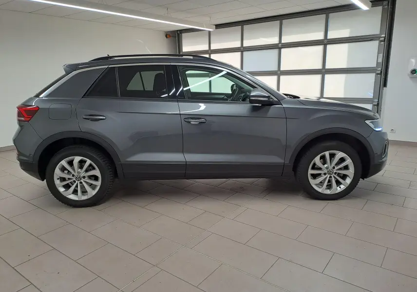 Profil droit du Volkswagen T-Roc 2024 gris Indium avec jantes alliage 17'' Johannesburg en intérieur showroom.