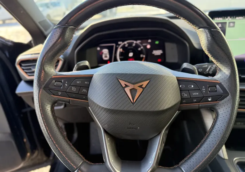 Vue rapprochée du volant en cuir noir perforé avec logo CUPRA cuivré du SUV Formentor 2023, tableau de bord numérique en arrière-plan.