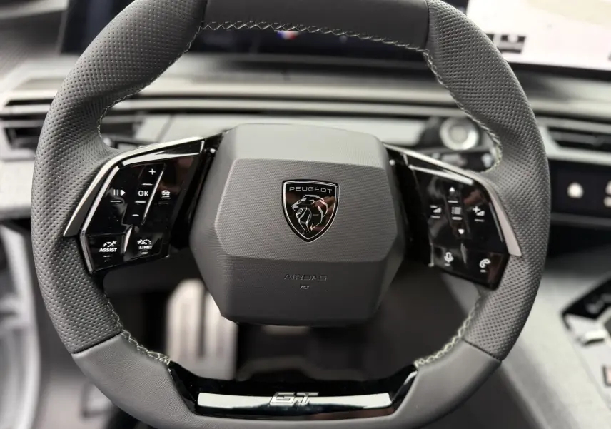 Gros plan sur le volant multifonction en cuir perforé noir du Peugeot 3008 Hybrid 2025 avec logo central et badge GT.