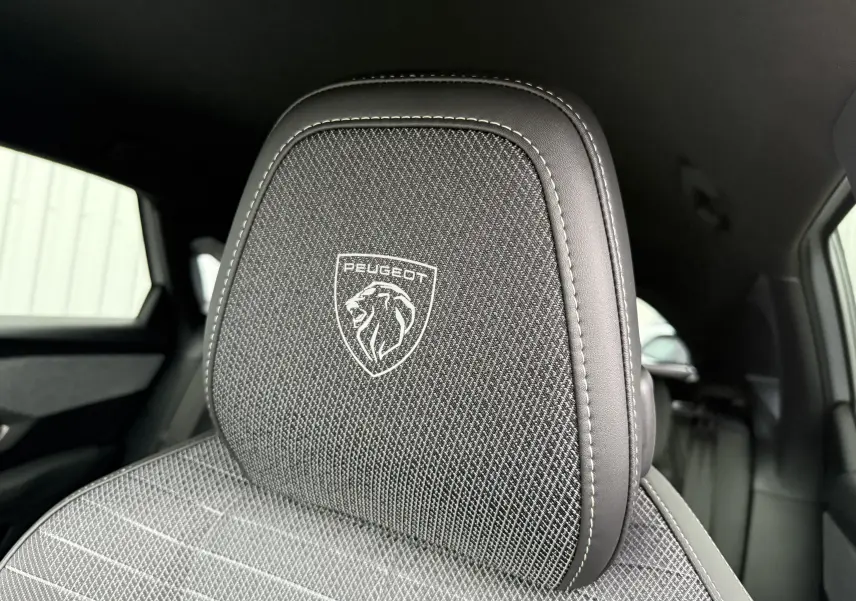 Gros plan sur l'appui-tête avant en tissu noir avec logo Peugeot brodé dans l'habitacle du 3008 hybride 2025.