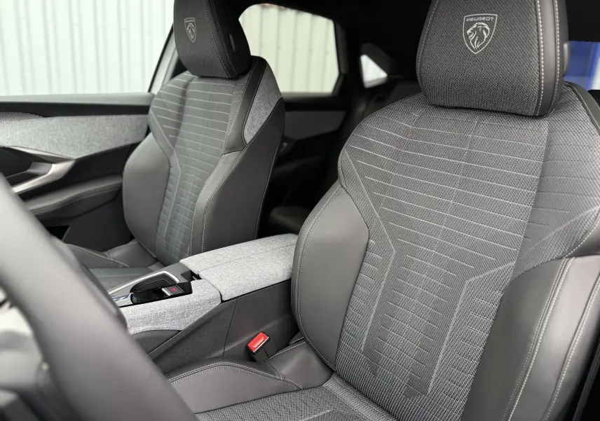 Gros plan sur les sièges avant gris et noir du Peugeot 3008 Hybrid 2025 avec logo lion brodé sur les appuie-têtes.