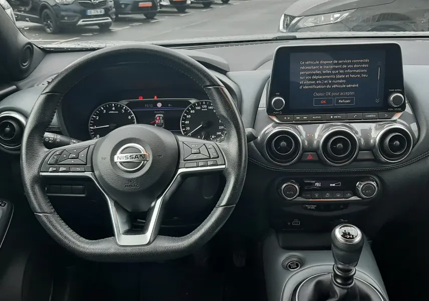 Vue intérieure centrée sur le volant et la console d'une Nissan Juke gris, avec boîte manuelle et écran tactile allumé.