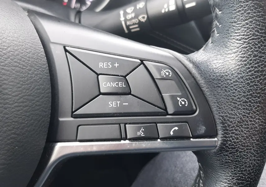 Gros plan sur les commandes de régulateur de vitesse au volant cuir noir du Nissan Juke gris, version 2020.