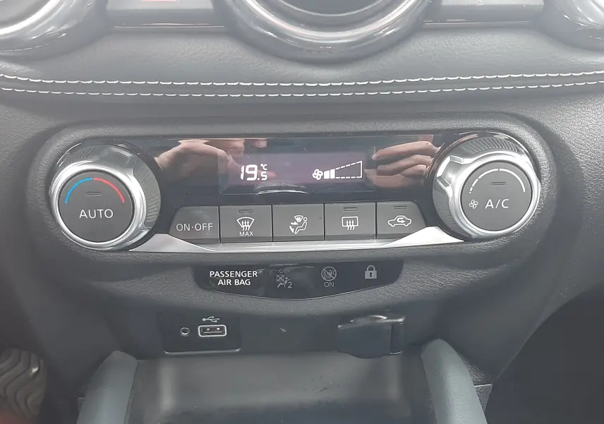 Vue rapprochée du tableau de bord noir du Nissan Juke 2020, mettant en valeur la commande de climatisation digitale à 19,5°C.