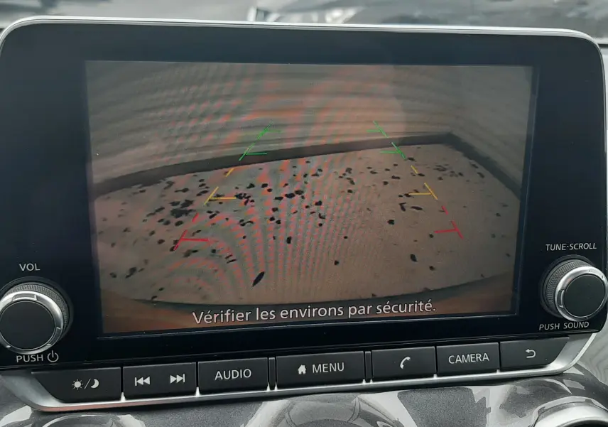 Écran central montrant la caméra de recul d’un Nissan Juke gris, avec les lignes de guidage colorées visibles.