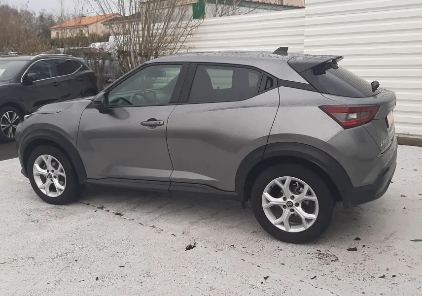 Nissan Juke gris vu de profil côté gauche, SUV compact avec jantes alliage et vitres teintées.