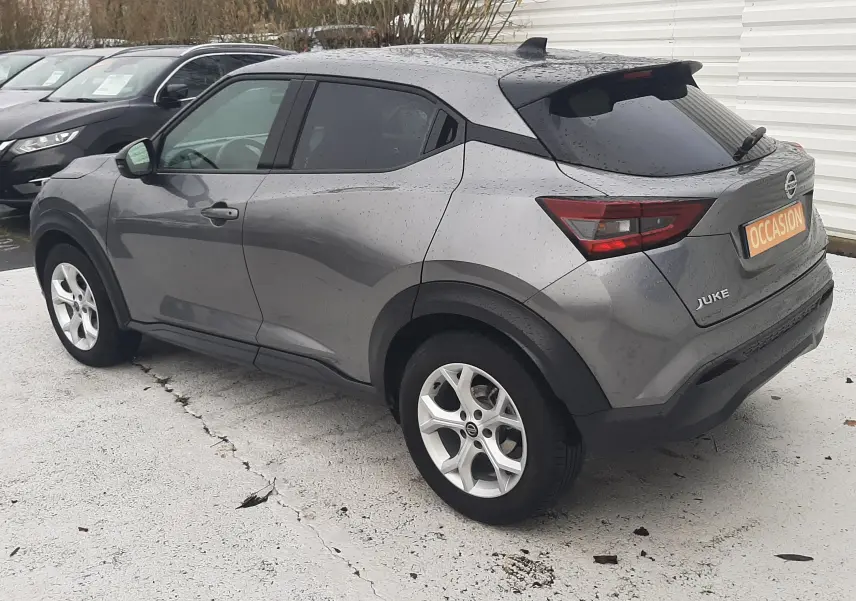 Vue 3/4 arrière droite d'un Nissan Juke gris 2020 avec jantes alliage et vitres teintées, stationné sur parking extérieur.