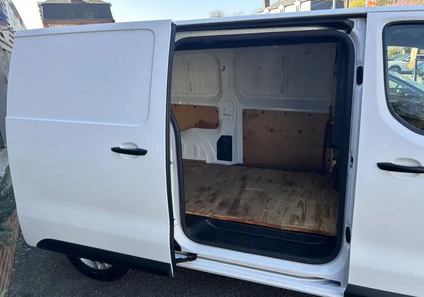 Vue latérale gauche d'un Citroën Jumpy blanc de 2017 avec porte coulissante ouverte révélant l'espace de chargement en bois.