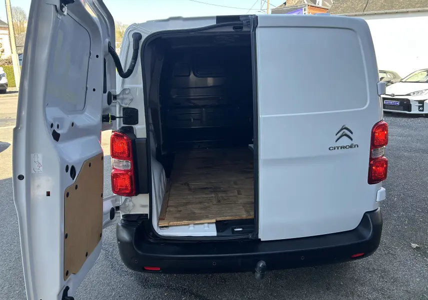 Vue arrière ouverte du Citroën Jumpy blanc montrant l'intérieur vide et un attelage visible sous le pare-chocs noir.