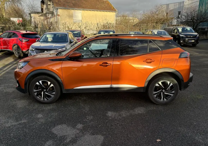Profil droit d’un Peugeot 2008 2021 en peinture métallisée Orange Fusion, soulignant ses lignes anguleuses et ses jantes noires.