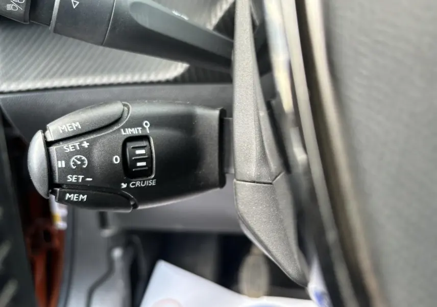 Gros plan sur la commande de régulateur de vitesse à gauche du volant dans l’habitacle du Peugeot 2008 Orange Fusion.