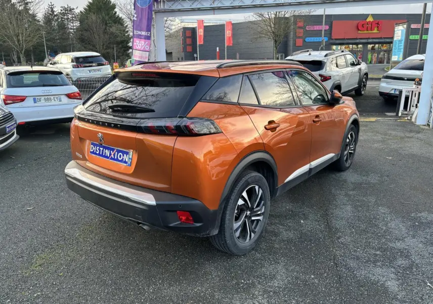 Vue 3/4 arrière droite d’un Peugeot 2008 orange fusion avec toit noir et jantes alliage bicolores sur parking.