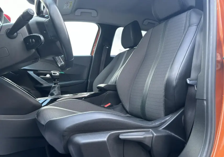 Vue intérieure côté conducteur du siège avant en tissu et cuir noir, avec porte orange fusion visible en arrière-plan.