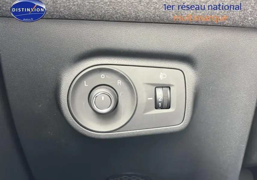 Gros plan sur les commandes grises de réglage des rétroviseurs et des phares du MG ZS Hybrid blanc, côté conducteur.