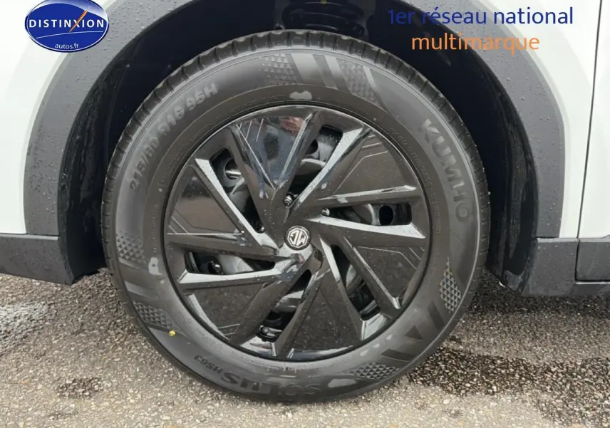 Gros plan sur la roue avant droite noire et brillante du MG ZS Hybrid blanc, avec logo MG au centre.