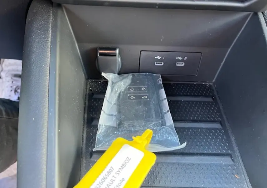 Gros plan sur la console centrale de la Renault Symbioz 2025 avec prises USB-C et clé dans un étui plastique.