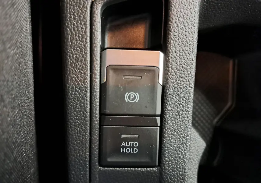Gros plan sur les boutons de frein de stationnement électronique et Auto Hold dans un Volkswagen T-Roc gris Indium 2024.