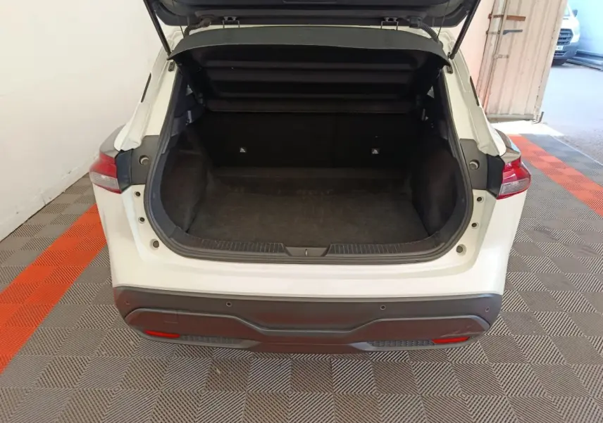 Coffre ouvert vu de l'arrière d'un Nissan Qashqai e-Power blanc, montrant l'espace de chargement vide et tapis noir.