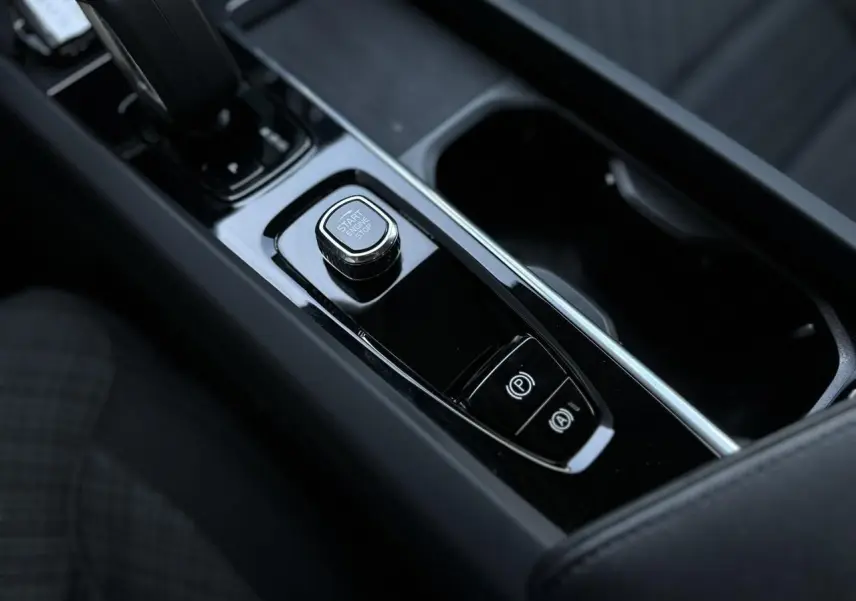 Gros plan sur la console centrale noire brillante du Volvo S60 B4 197 DCT7 MHEV Core+ avec bouton start/stop et frein électronique.