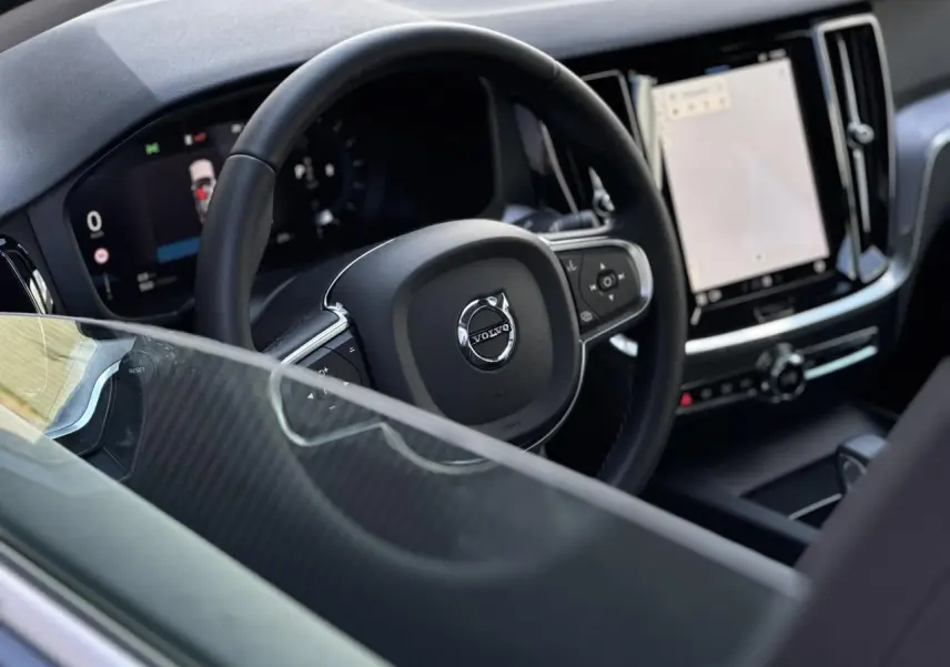 Vue intérieure centrée sur le volant noir et le tableau de bord numérique du Volvo S60 gris Thunder 2024.