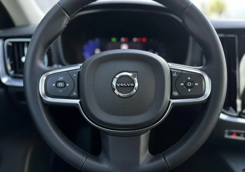 Gros plan sur le volant noir de la Volvo S60 2024 avec commandes intégrées et logo central chromé.