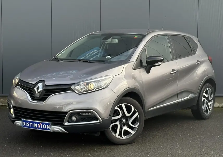 Renault Captur gris Cassiopée en 3/4 avant droit, avec jantes alliage noires et phares allumés.