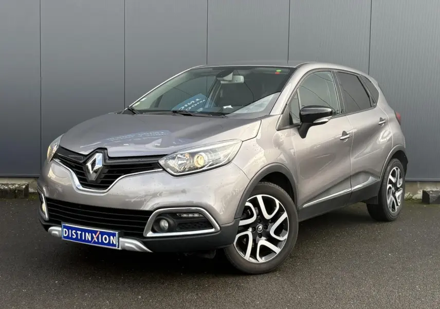 Renault Captur gris Cassiopée en 3/4 avant droit, avec jantes alliage noires et phares allumés.