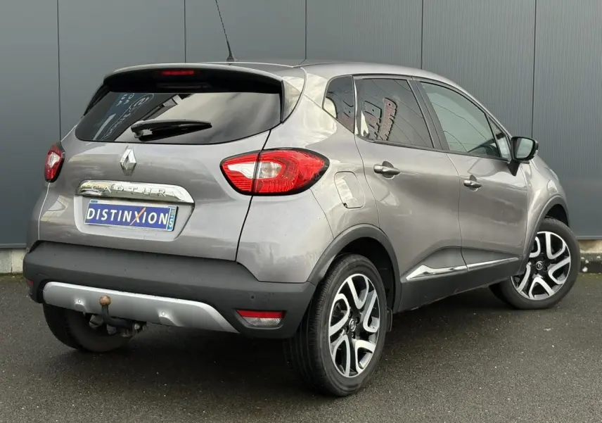 Vue 3/4 arrière droite d'un Renault Captur gris Cassiopée avec jantes alliage noires et attelage visible.