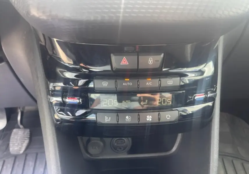 Gros plan sur la console centrale noire brillante de la Peugeot 208 avec commandes climatisation et affichage digital.