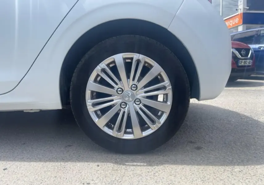 Gros plan sur la jante alliage 16 pouces Titane Technical Grey côté arrière droit d'une Peugeot 208 blanc perle texture.