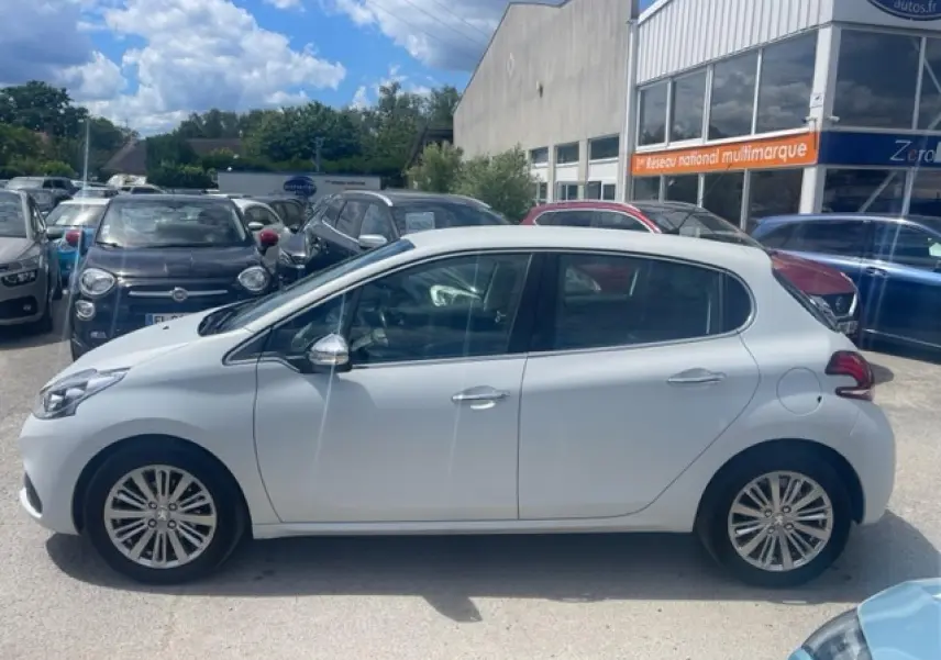 Profil côté gauche d'une Peugeot 208 blanc perle avec jantes alliage 16 pouces, stationnée en extérieur.