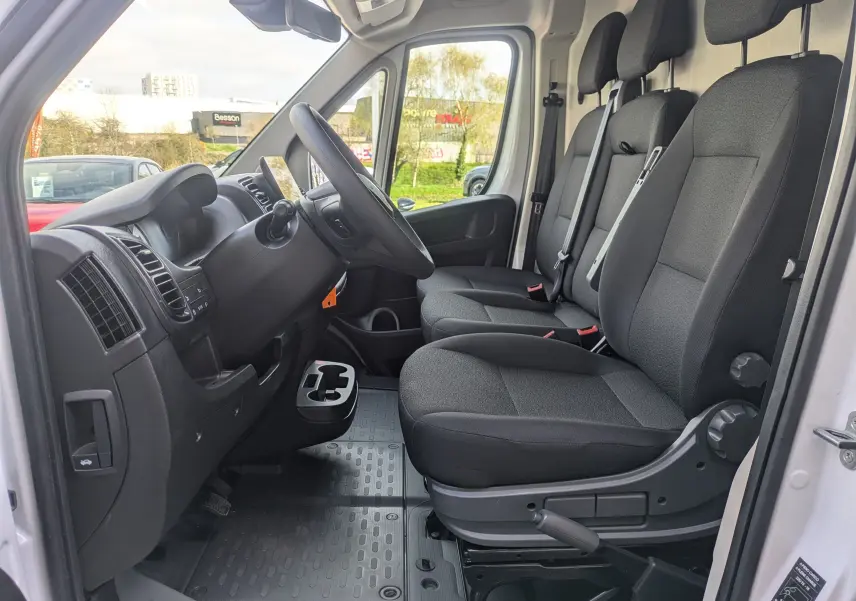 Vue intérieure côté conducteur du Peugeot Boxer Fourgon blanc 2025, montrant les sièges noirs et le tableau de bord.
