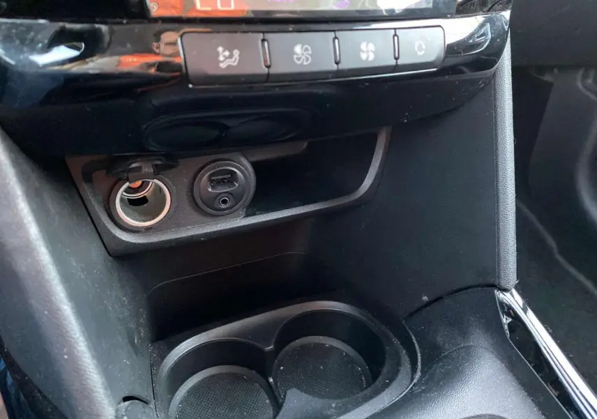 Gros plan sur la console centrale noire du Peugeot 2008 avec prise USB, allume-cigare et commandes de climatisation.