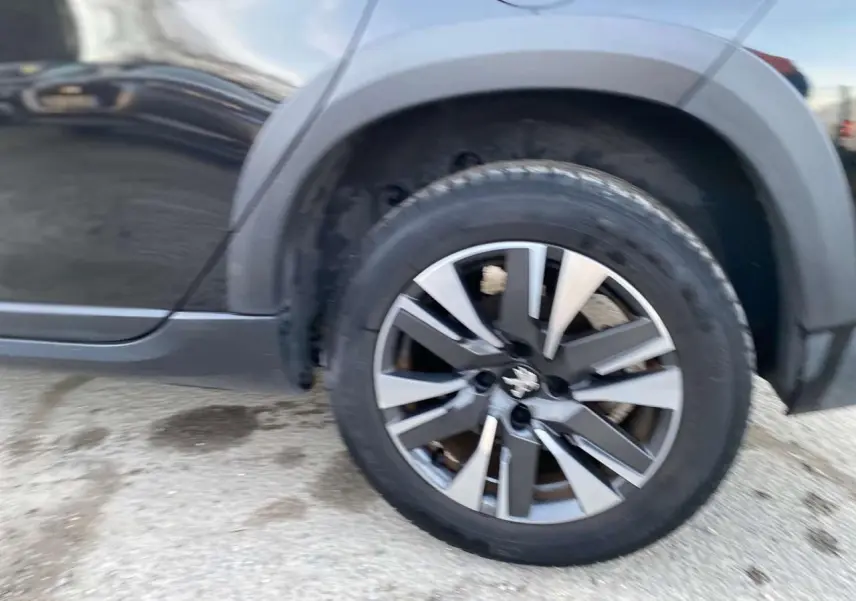 Gros plan sur la roue avant droite d’un Peugeot 2008 noir Perla Nera avec jante aluminium diamantée gris.