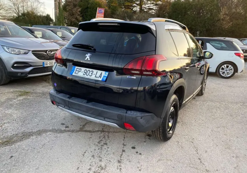 Peugeot 2008 noir Perla Nera vue 3/4 arrière droit, avec feux arrière rouges et toit avec barres de toit.