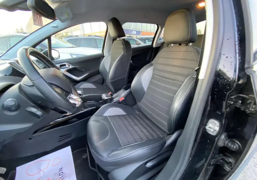 Vue intérieure côté conducteur du Peugeot 2008 noir Perla Nera, sièges sport avec surpiqûres blanches et volant cuir.