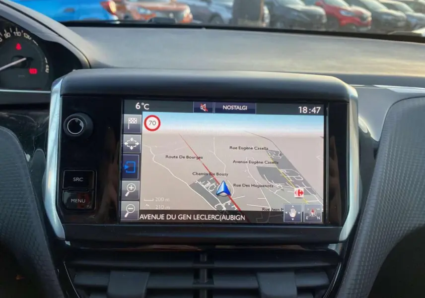Vue intérieure centrée sur l'écran tactile du GPS du Peugeot 2008, avec tableau de bord et voitures en arrière-plan.