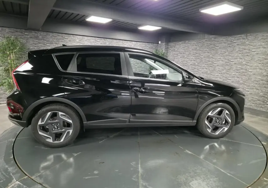 Vue de profil côté gauche d'un Hyundai Bayon noir 2025 avec jantes alliage 17 pouces dans un showroom intérieur.