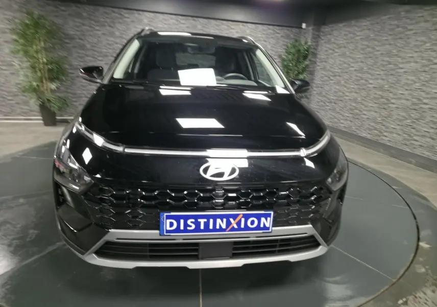 Vue avant d'une Hyundai Bayon 2025 noire avec calandre noire laquée et plaque Distinxion en intérieur showroom.