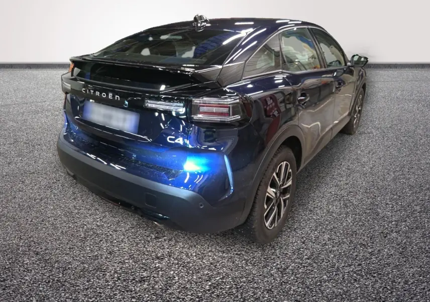 Vue 3/4 arrière droite d'une Citroën C4 hybride 2025 bleu foncé avec feux arrière LED et spoiler de coffre.
