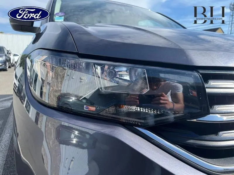 Gros plan sur le phare avant gauche gris cendré métallisé du Volkswagen T-cross 2022 avec calandre chromée.